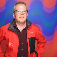 Niel Nielsen portræt. Person med rød jakke på farverig rød og blå baggrund.